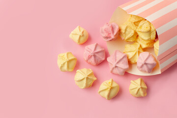 Merengues caseros rosas y amarillo junto a una caja de cartón con rayas rosas sobre un fondo rosa pastel. Vista superior y de cerca. Copy space