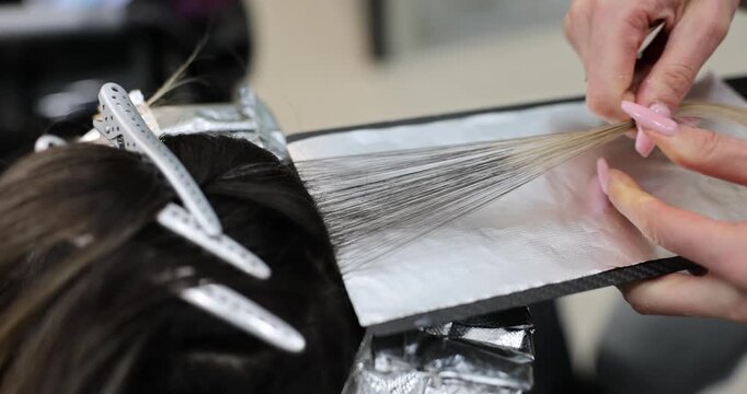Colorist pulls strand of hair over foil before applying dye