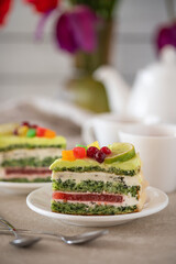 A colorful layered cake slice with green frosting, red berries, and yellow citrus slices on a white plate