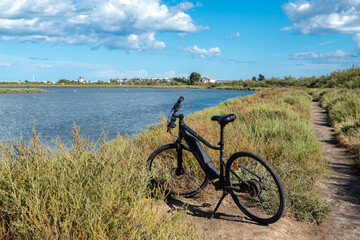 un vélo électrique posé au bord d'un étang, de Camargue sous un ciel bleu 
