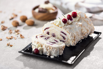 Sliced cream roll with berries on a black plate, dusted with powdered sugar.