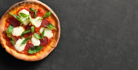 Pizza with mozzarella, pepperoni, tomato sauce and basil on dark background with free space