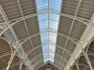 Interior view of a historical market hall with a glass roof, showcasing architectural details and the interplay of light and shadow in Valencia, Spain.