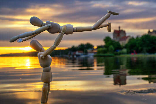 Lustiges Foto von Holzpuppen, die im Wasser eines Sees eine Hebefigur bei Sonnenuntergang machen