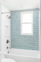 A bathroom shower detail with white and light blue subway tiles, white tub, and bronze shower head and faucet.