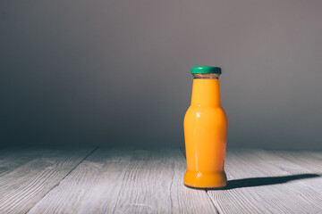 A glass bottle of orange juice is sitting on a wooden table