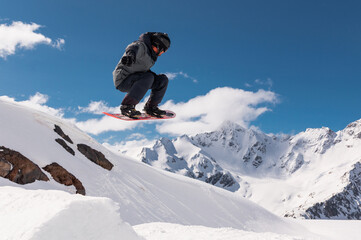 Jumping snowboarder holds one hand on a snowboard against the background of a blue sky and large...