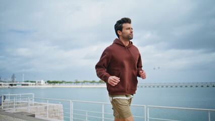 Focused runner training river bank in cloudy morning. Fitness guy running bay