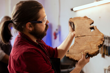 Manufacturer respecting safety codes doing last touches on piece of wood before using it for furniture assembly. Woodworking specialist examining timber block for damages