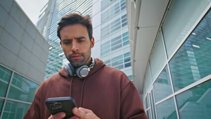 Confused guy reading smartphone message on city street. Closeup bearded man