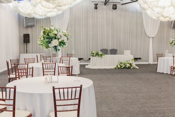 Decorated interior for festive event. Fancy table set for dinner with white flower composition in restaurant, luxury interior background. Wedding elegant banquet decoration arranged by catering