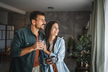 Portrait of couple stand with coffee and water, watch intro the window