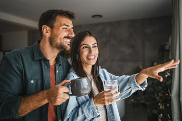 Portrait of couple stand with coffee and water, watch intro the window
