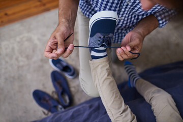 Help, father and child tie shoes in bedroom for preparation, morning routine or getting ready on weekend. Top view, sneakers and man with kid for learning, growth development or support in home - Powered by Adobe