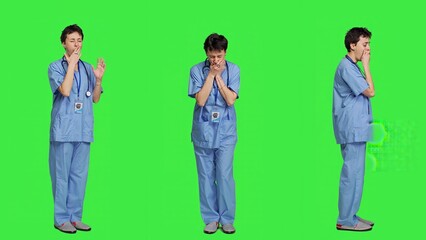 Obraz premium Medical assistant feeling extremely sleepy against greenscreen backdrop, being overworked after the night shift. Woman nurse yawns and feels exhausted in studio, burnout and anxiety. Camera A.