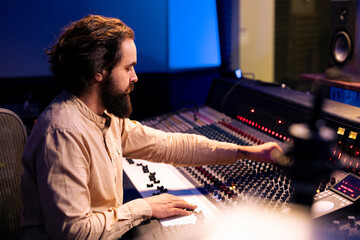 Music producer editing and mixing tunes in control room, working on a new song in professional...