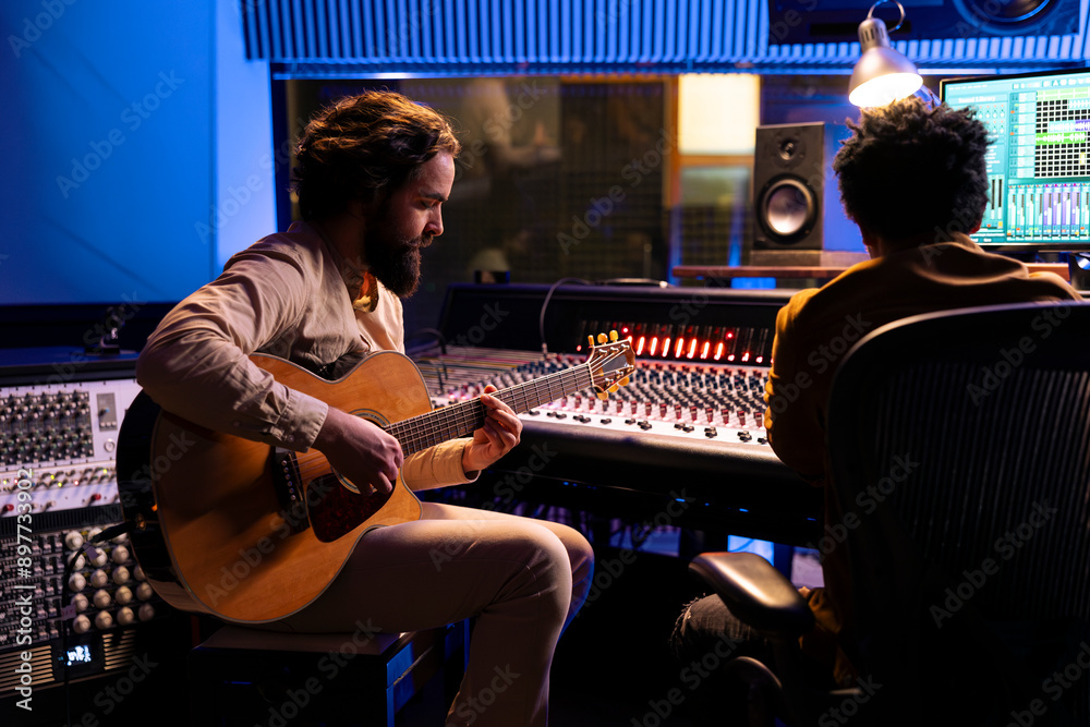 Poster singer creating a new hit song in studio with guitar running, working with audio expert to produce m