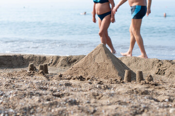 Sand pyramid on the beach by the sea, Two people walking along the edge of the water in the background, Summer vacation in a tropical country