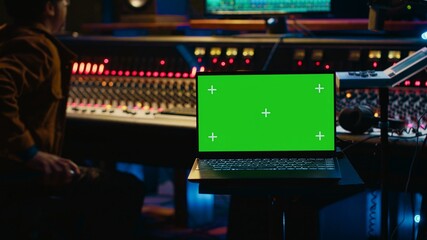 Skilled audio technician processing and mixing sounds next to mockup display on laptop, using...