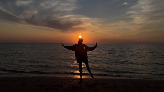 The silhouette of a girl dancing on the sand against the background of sunset and the horizon of the sea. 4k video. High quality 4k footage.