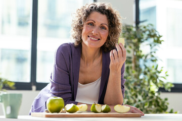 Pretty mature woman eating an apple in the kitchen at home