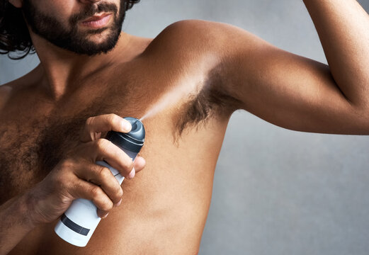 Armpit, deodorant and man with spray in studio for wellness, grooming and body hygiene on gray background. Skincare, health and person with aerosol for fragrance, cosmetics and products for underarm