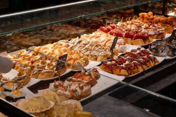Typical snacks of Basque Country, variety of pinchos or pinxtos oven baked sea food, bread, skewers with jamon, goat cheese served in bar in San-Sebastian or Bilbao, Spain, close up
