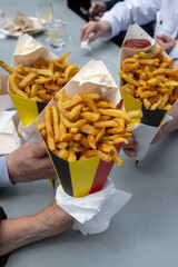 Fototapeta premium Belgian street and fast food, paper cone bag in colors of Belgian flag with fried potato frit chips and mayonnaise sauсe.