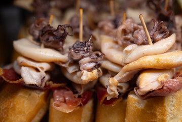 Typical snack of Basque Country, pinchos or pinxtos skewers with small pieces of bread, sea food, eggs, cheese, jamon served in bar in San-Sebastian or Bilbao, Spain, close up