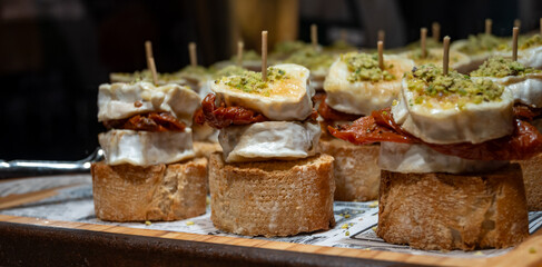 Typical snack of Basque Country, pinchos or pinxtos skewers with small pieces of bread, sundried tomatoes, goat cheese served in bar in San-Sebastian or Bilbao, Spain, close up