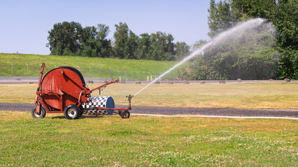 Traveling sprinkler hose reel irrigation machine watering a park field.