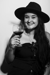 Black and white portrait of beautiful woman in hat holding glass of wine.