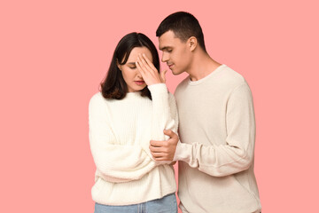 Naklejka premium Young man consoling upset woman on pink background