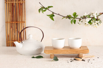 Wooden stand with teapot, cups, spoon of dry tea and leaves on light background