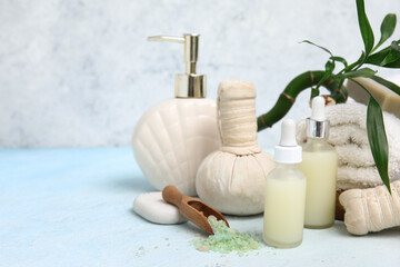 Set of spa supplies with bottles of cosmetic oil, sea salt, towel and herbal bags on light blue table