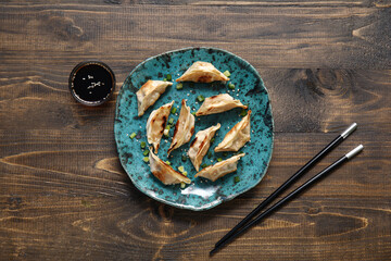 Plate with fried Japanese gyoza and bowl of soy sauce on wooden background
