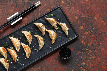 Black board with fried Japanese gyoza and bowl of soy sauce on dark background