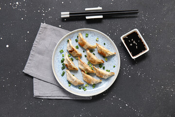 Plate with fried Japanese gyoza and bowl of soy sauce on black background