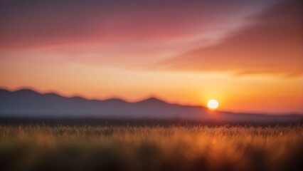 Fototapeta premium A blurry sunset over a field of grass with mountains in the distance, out of focus