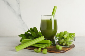 Glass of celery juice with whole and chopped celery on white background