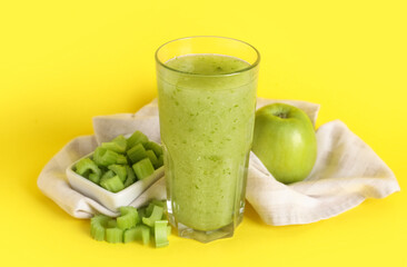 Glass of celery juice with chopped celery and apple on yellow background