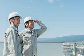 青空の中に立つ作業服を着た作業員（建設・建築・設計・不動産・土木・工事・現場監督・運送）
