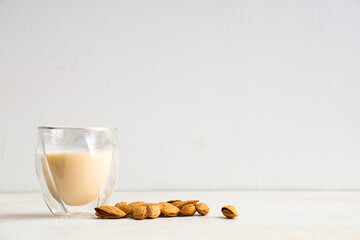 Glass of fresh almond milk and nuts on white background