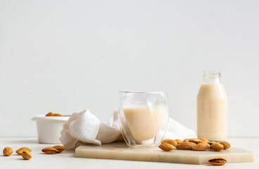 Glass and bottle of fresh almond milk with nuts on white background