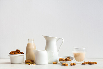 Jugs and bottle of fresh almond milk with nuts on white background