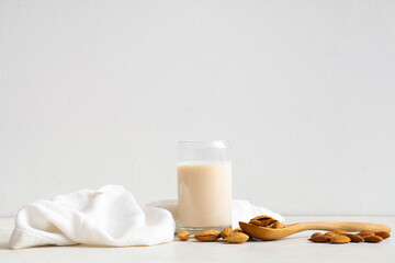 Glass of fresh almond milk and spoon with nuts on white background