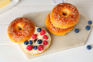 Board of tasty bagels with berries and butter on white wooden background