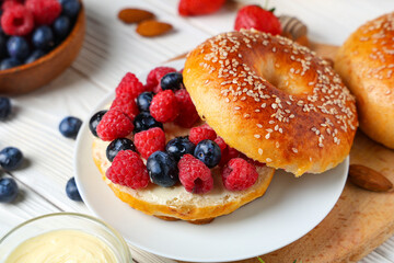 Plate of tasty bagel with butter and berries on white wooden background