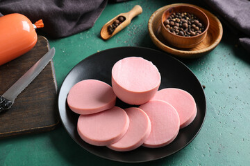 Plate with slices of tasty boiled sausage and peppercorns on grunge green background © Pixel-Shot