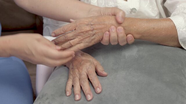 Female caregiver assisting massage and apply lotion on elderly hand for moistering dry skin